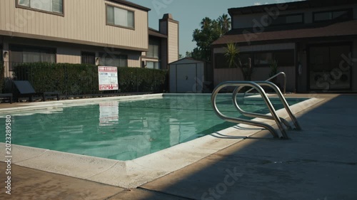 Corner view of empty pool with clean water, metal rails and sign reflection, apartment complex and laundry room in background
