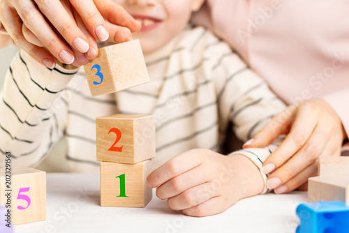 Mother or teacher helping child with math using wooden numbers blocks. Concept of early childhood education, mental development and homework support at home.