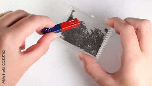 Tableau sur toile Hands Holding Bar Magnet Over Case of Iron Filings