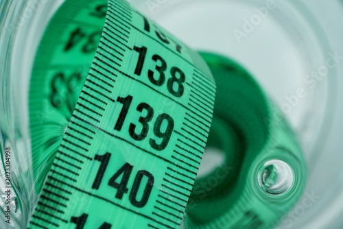 Macro close-up of a green measuring tape coiled inside a transparent container