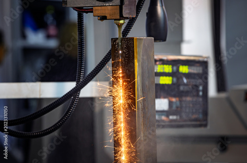 Wire EDM cutting of metal workpiece with sparks in industrial machine.