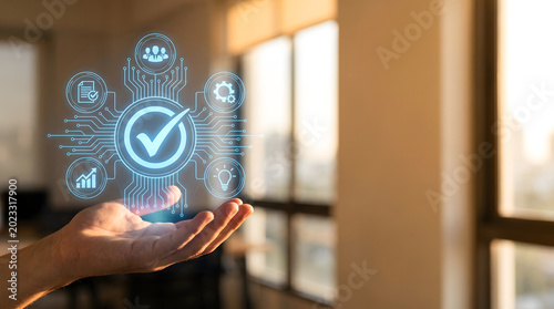 Quality assurance and standard compliance concept. Hand holding a glowing virtual checkmark hologram with business process icons in a modern office.