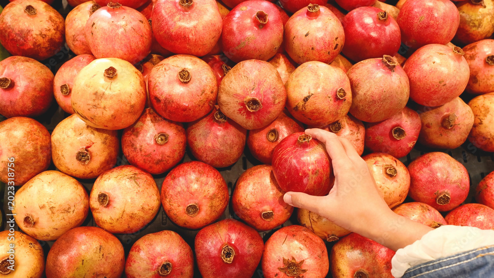 Obraz premium Hand Selecting a Fresh Red Pomegranate from a Vibrant Market Display
