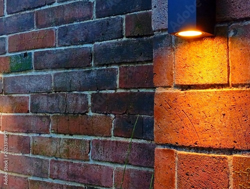 Warm Glowing Sconce Light on Red Brick Corner Wall, Modern Exterior Lighting on Rustic Brick Background