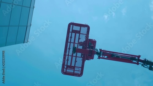 A boom lift for conveniently lifting the basket with workers to heights, against the glass building and a blue sky. Shot in motion 