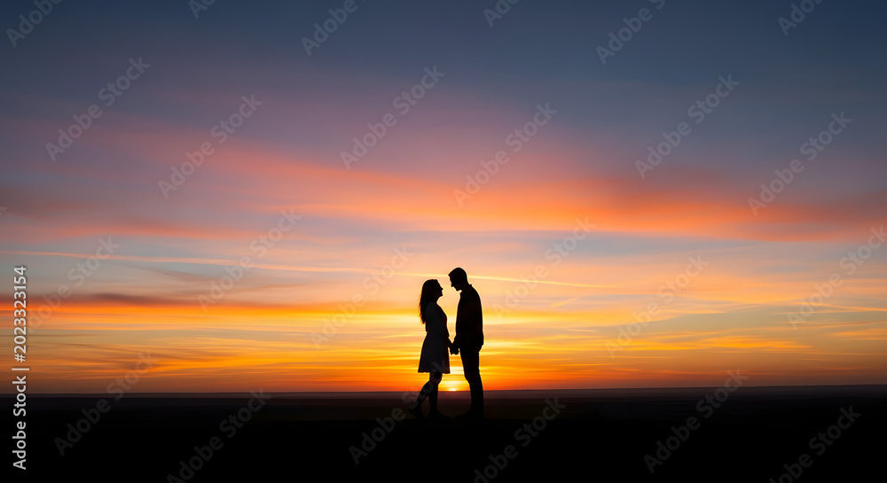 Fototapeta premium A silhouette of a couple holding hands against a vibrant orange and purple sunset sky
