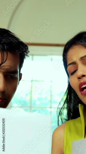Indian asian young couple having heated discussion on finance with documents while sitting at kitchen counter in modern Indian home looking stressed and frustrated while managing Indian budget