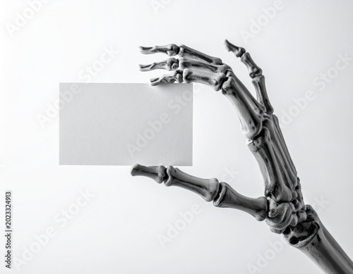 Skeleton hand is holding a blank white business card or a message board against a simple bright background offering space for text or design