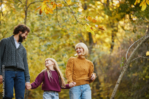A joyful family strolls through a park on a weekend afternoon. Golden autumn leaves create a beautiful backdrop as they share laughter and engage in conversation.
