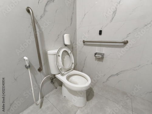 Clean accessible restroom toilet with stainless steel grab bars for disabled or elderly people in a hospital or clinic with marble wall background.