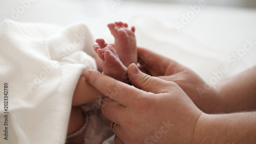 A pair of tiny newborn feet rests gently in the hands of an adult. Soft surroundings create a warm atmosphere.