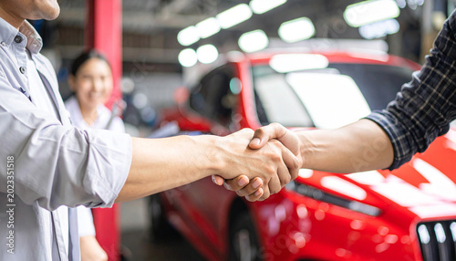 Hands of happy car owner discussing vehicle repair with mechanic beside bright red car trust and positive customer experience in well lit contemporary automotive workshop 