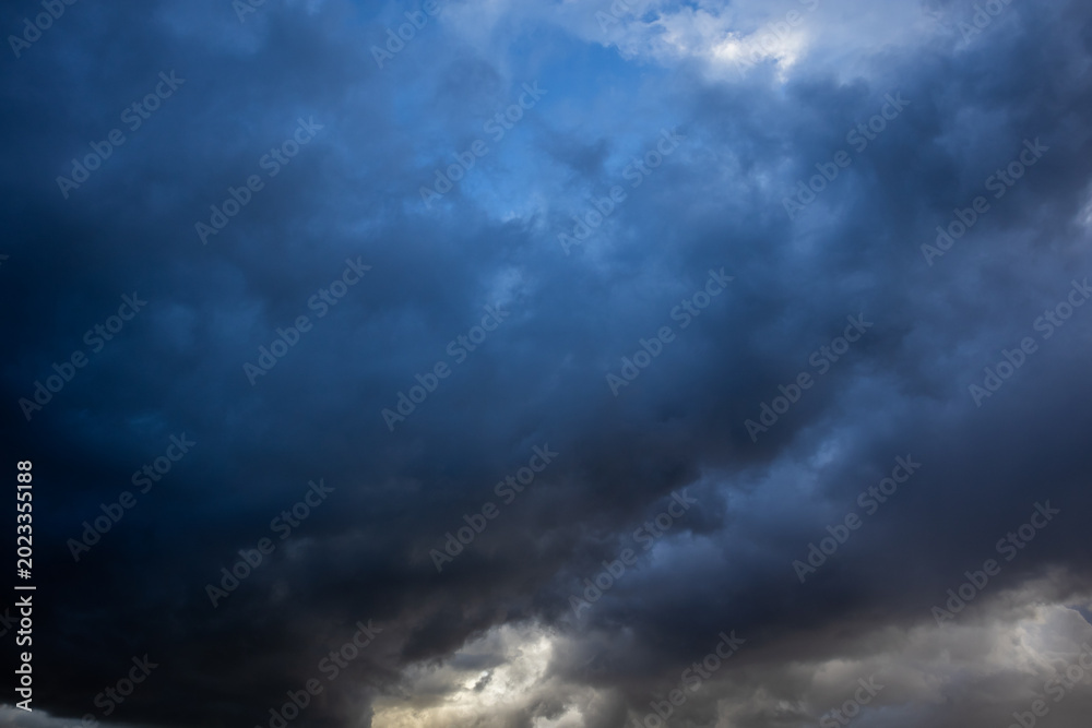 Obraz premium Dramatic dark storm clouds filling the sky with brooding blue-grey tones and glimpses of light breaking through below