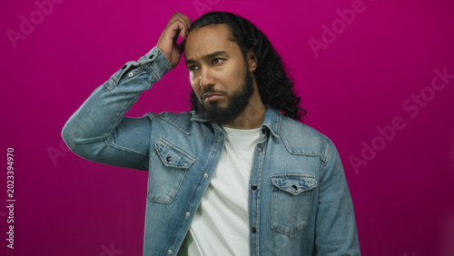 Bild auf Leinwand Young hispanic arab man scratching his head with hand in studio against magenta backdrop; confusion doubt reflection