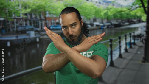 Fényképezés Man wearing volunteer t shirt crossing arms in x gesture on canal street in amsterdam; rejection boundary resolve