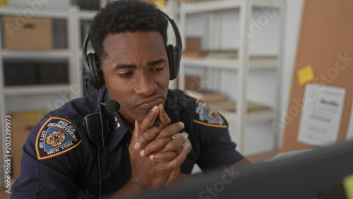 Foto Man police officer with headset, hands clasped at mouth while watching a monitor at building dispatch desk; duty concern