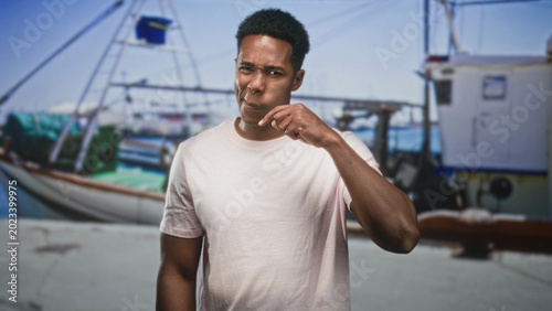 Obraz na płótnie Man touching mouth with finger beside fishing boat on dock, hand near lips and pained expression; disgust unease