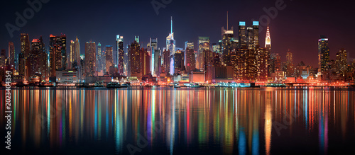 A vibrant nighttime cityscape, illuminated by a myriad of lights, mirroring in the calm water below, creating a stunning reflection