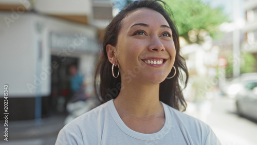 Photography Young hispanic woman smiling with face turned upward on a sunlit city street; contentment reflection