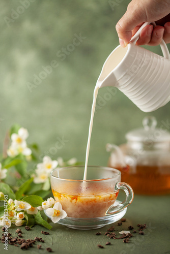 Composition with cup of jasmine milk tea and flowers on green background