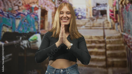 Foto Woman with clenched fists and exposed midriff in a graffiti covered stairwell on a street, smiling in a victory pose; triumph hope