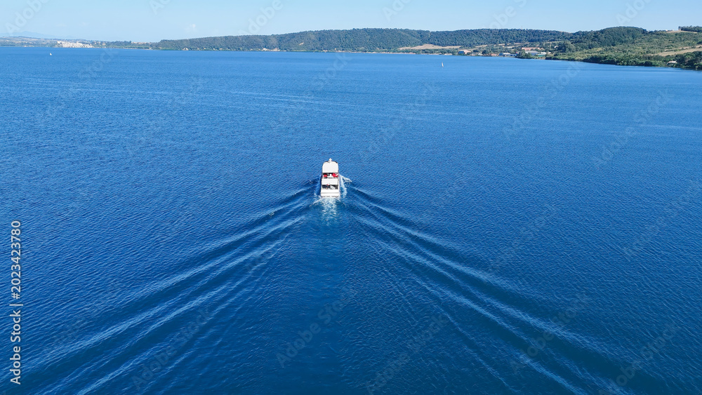 Fototapeta premium Serenity in motion as a lone boat glides across the tranquil blue waters under the sunlit sky of a beautiful afternoon