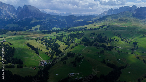Vast green valleys nestled among majestic mountains under a dramatic sky in the Dolomites during the golden hour