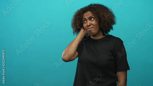 Canvastavla Woman with hand on neck and raised eyebrow in studio against a teal wall showing a puzzled expression; confusion