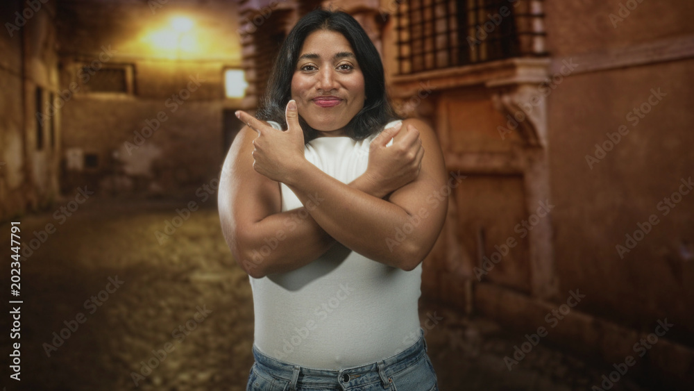Naklejka premium Woman crossing arms over chest showing forearms and pointing fingers in a narrow cobblestone alley at night; confidence.