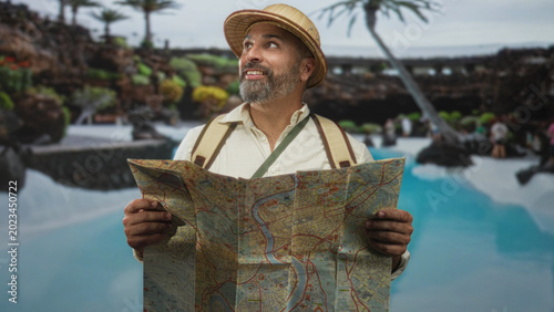 Canvastavla Man holding map and looking up at pool with hands visible, wearing straw pith hat and backpack while standing near water and rocks; wanderlust exploration