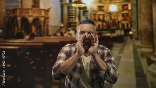 Cuadro en lienzo Man cupping hands around mouth shouting toward the nave in a church aisle beside wooden pews and stone pillars; anger protest