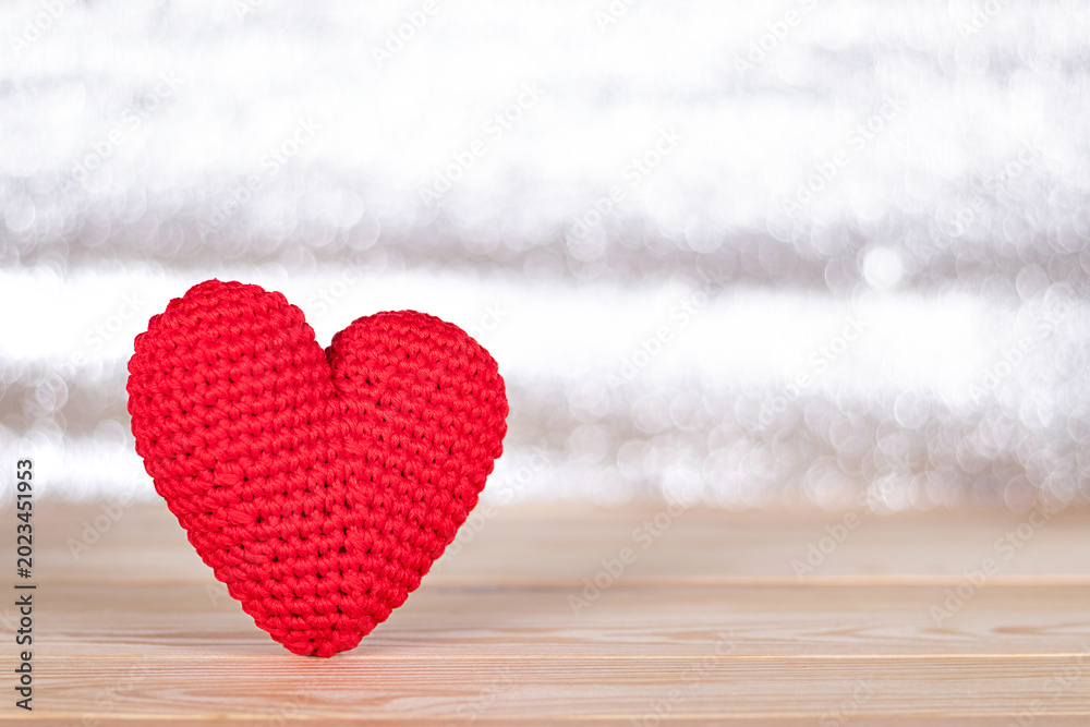 Fototapeta premium Red crocheted heart standing on a wooden surface against a light blurred background.