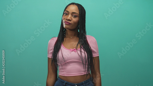 Φωτογραφία Woman smiles and tilts head with midriff visible in pink crop top against teal studio wall, hands relaxed at sides; confidence warmth