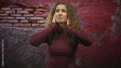 Εκτύπωση καμβά Young woman with curly hair pressing hands to ears and closing eyes against imagined noise in studio; anxiety