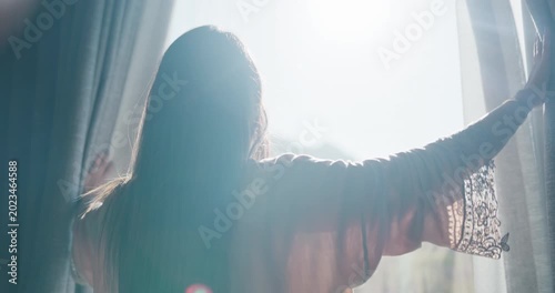 Woman, light and open with curtains in bedroom for morning, stretching or new day in home. Back view, female person or awake with fabric, flare or window for outdoor sunlight, rise and shine in house