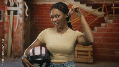 Foto Woman holds pink striped helmet and car keys aloft inside a building under construction, smiling while showing the keys; confidence