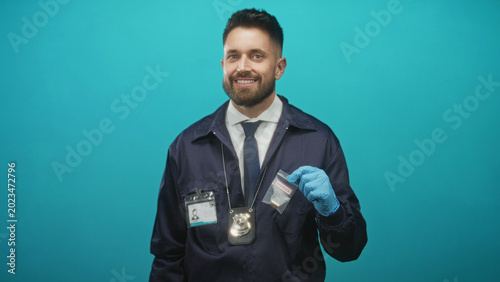 Photos Man detective with beard wearing badge and tie, blue gloved hand holding an evidence bag with a bullet casing in a studio; confidence duty