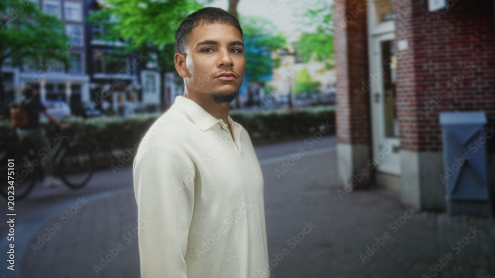 Obraz premium Man walking in profile with face visible past a brick building on street wearing a white sweater; calm reflection.
