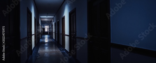 Dark, narrow hallway with many closed doors leads towards light. Eerie atmosphere, suspense, mystery. Creepy interior, abandoned building, school, hospital setting. Long corridor.