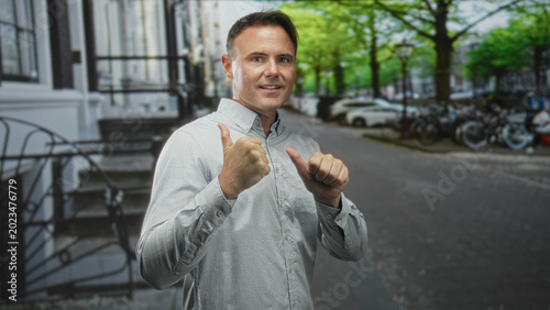 Man with thumbs pointing to chest on a street by bicycles and stairs; confidence approachability.