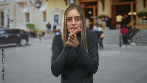 Photos Young hispanic woman clapping hands near a building entrance on a busy city street with steps and parked car; determination resolve confidence