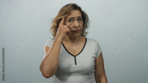 Slika na platnu Hispanic woman pointing finger to temple in studio portrait wearing striped shirt; thoughtfulness introspection