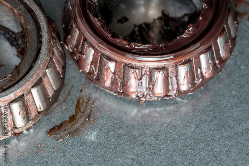 Dirty mechanical bearings lie on a grimy surface. Oil and grime stain the metal components. They show signs of heavy use and wear. Industrial repair or maintenance work suggests context