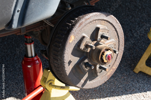 Rusted wheel hub with bolts and central cap. Red cap gleams under bright sunlight. Surface shows signs of heavy use and wear. Ideal for automotive repair or machinery themes. Highlights durability