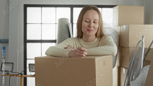 Fotografía Woman holding keys aloft above stacked cardboard boxes, hand raised and smiling amid moving supplies in a bright studio; new home relief
