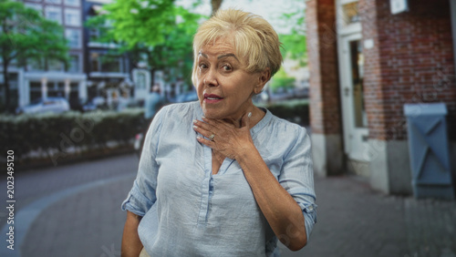 Foto Senior hispanic woman touching chest with hand on city street by brick storefront and bicycle; concern vulnerability