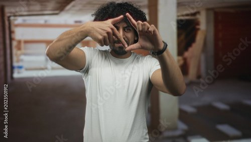 Quadro su tela Man frames face with fingers and thumbs making a viewfinder gesture in a building construction site, bare forearms visible; creative idea