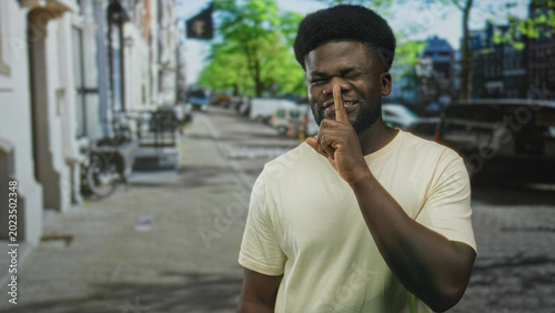 Tableau sur toile Man pressing finger to lips for silence on city street, wearing light t shirt and subtle smirk; playful mischief