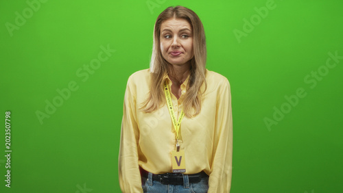 Konstfotografi Woman wearing yellow shirt and volunteer visitor card with lanyard, face visible and pursing lips while glancing sideways in studio; skeptical