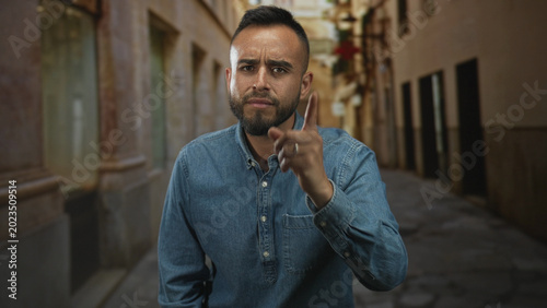 Bilde på lerret Man points finger to camera on narrow old town street, furrowed brow and raised hand showing a ring; anger warning
